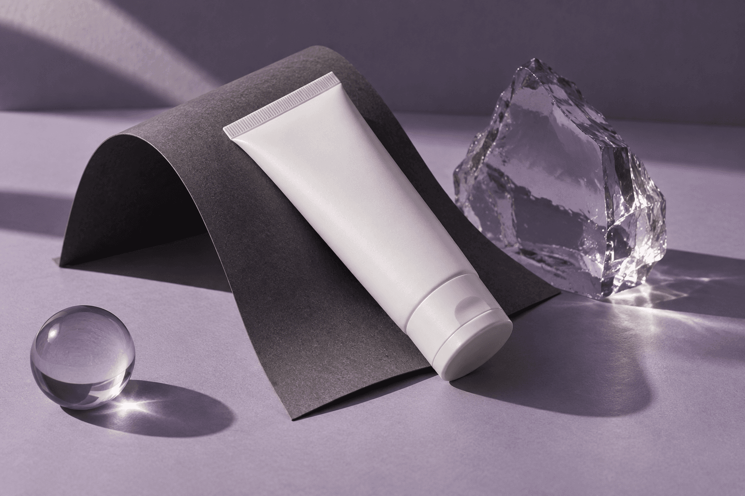 White cream tube, folded graphite paper and lavender glass in evening light